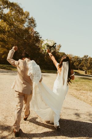 Joyful newlyweds celebrating outside raising arms with bouquet after rustic barn wedding.