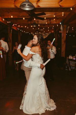 Bride and groom share a romantic slow dance under warm string lights at their rustic barn wedding reception.