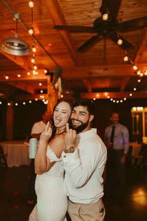 Bride and groom smile and pose playfully together on the dance floor at their rustic wedding reception.