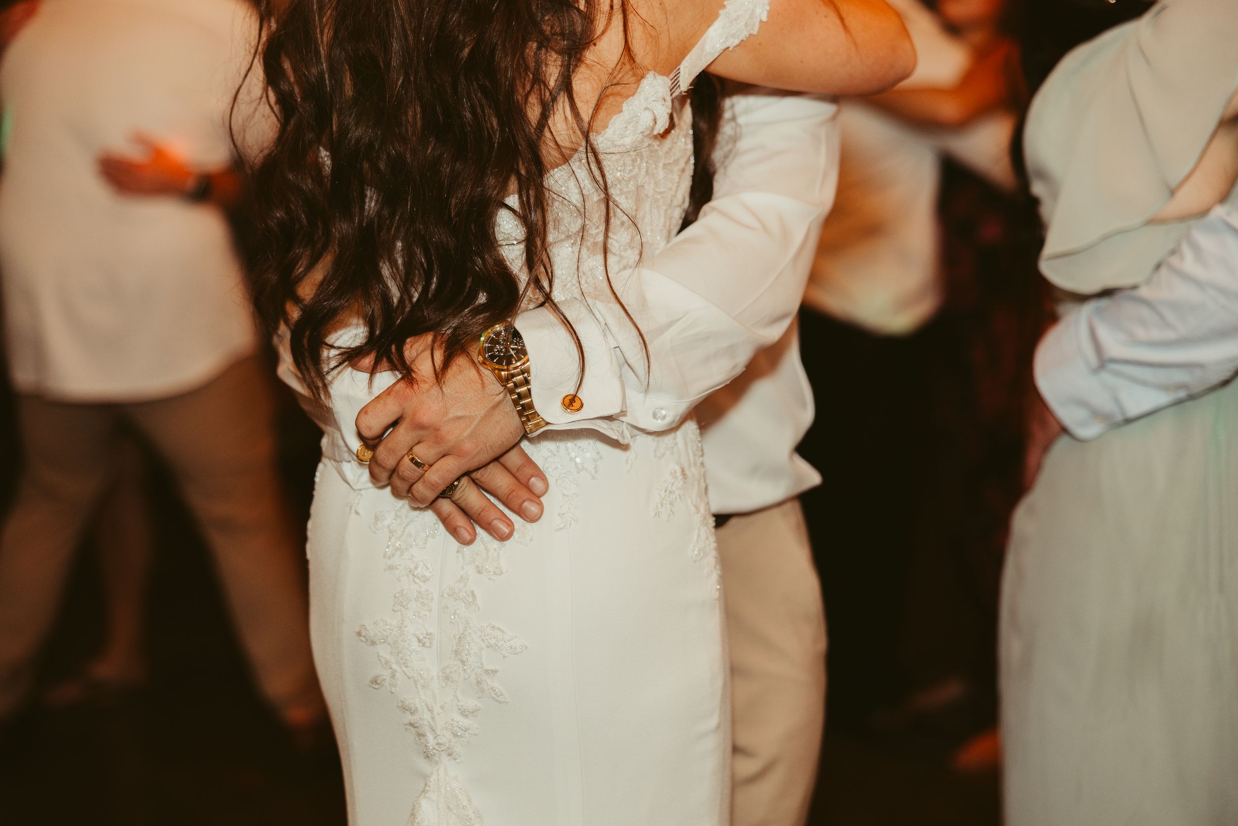 Bride and groom share a slow dance, hands clasped together at a wedding reception.
