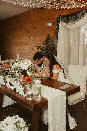 Bride and groom share an intimate moment seated at a floral-decorated sweetheart table at their rustic barn wedding reception.