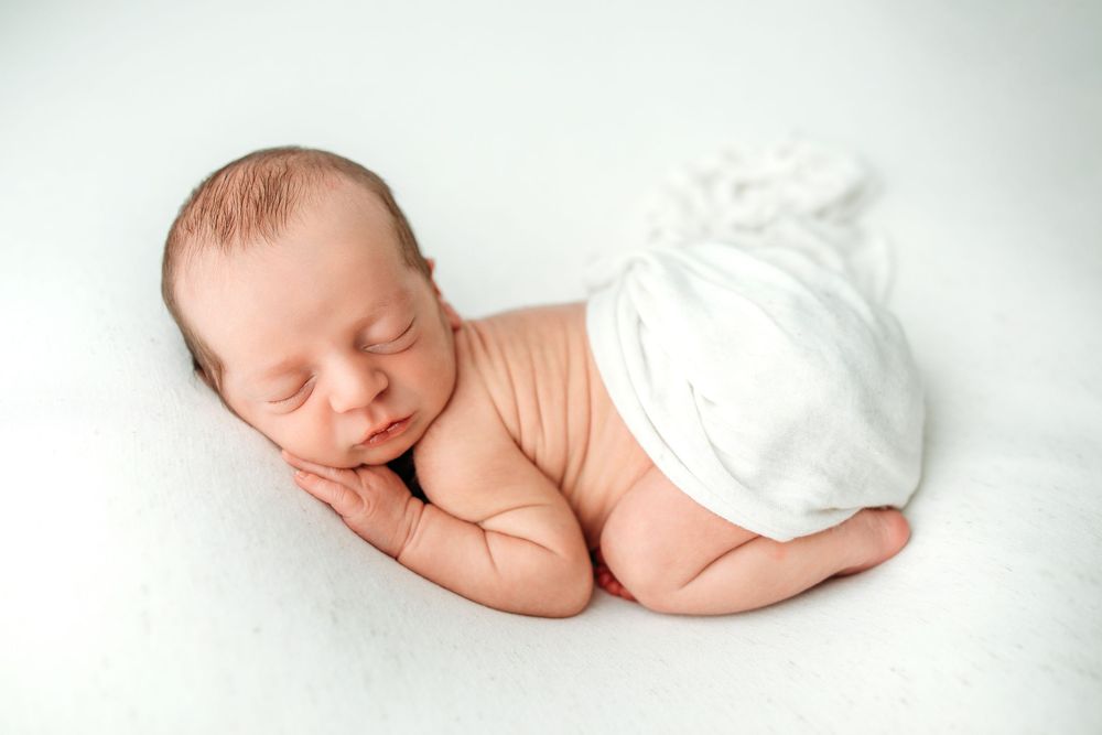 A sleeping newborn baby lies peacefully on white fabric in various gentle poses.