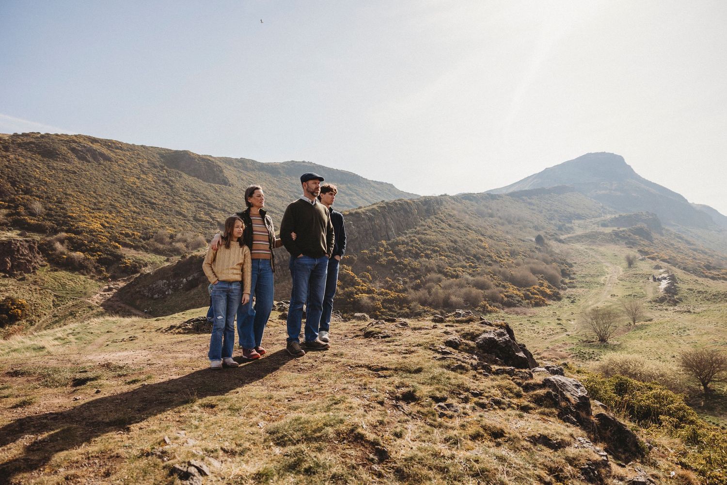 Hikers explore scenic mountain trails with rugged terrain and rolling hills in the distance on a cloudy day.