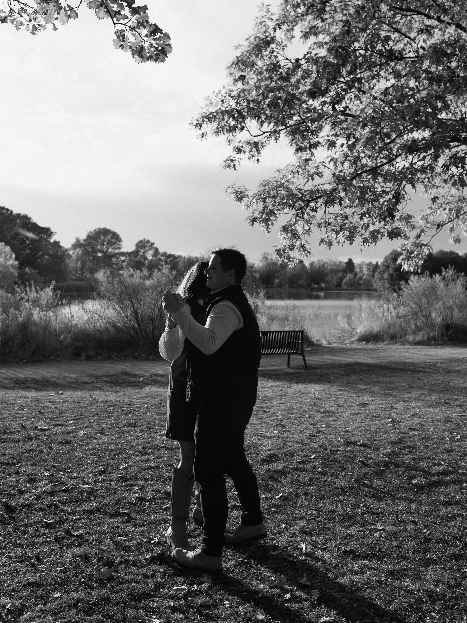 Black and white photo series of a romantic couple embracing in a sunlit autumn park setting.