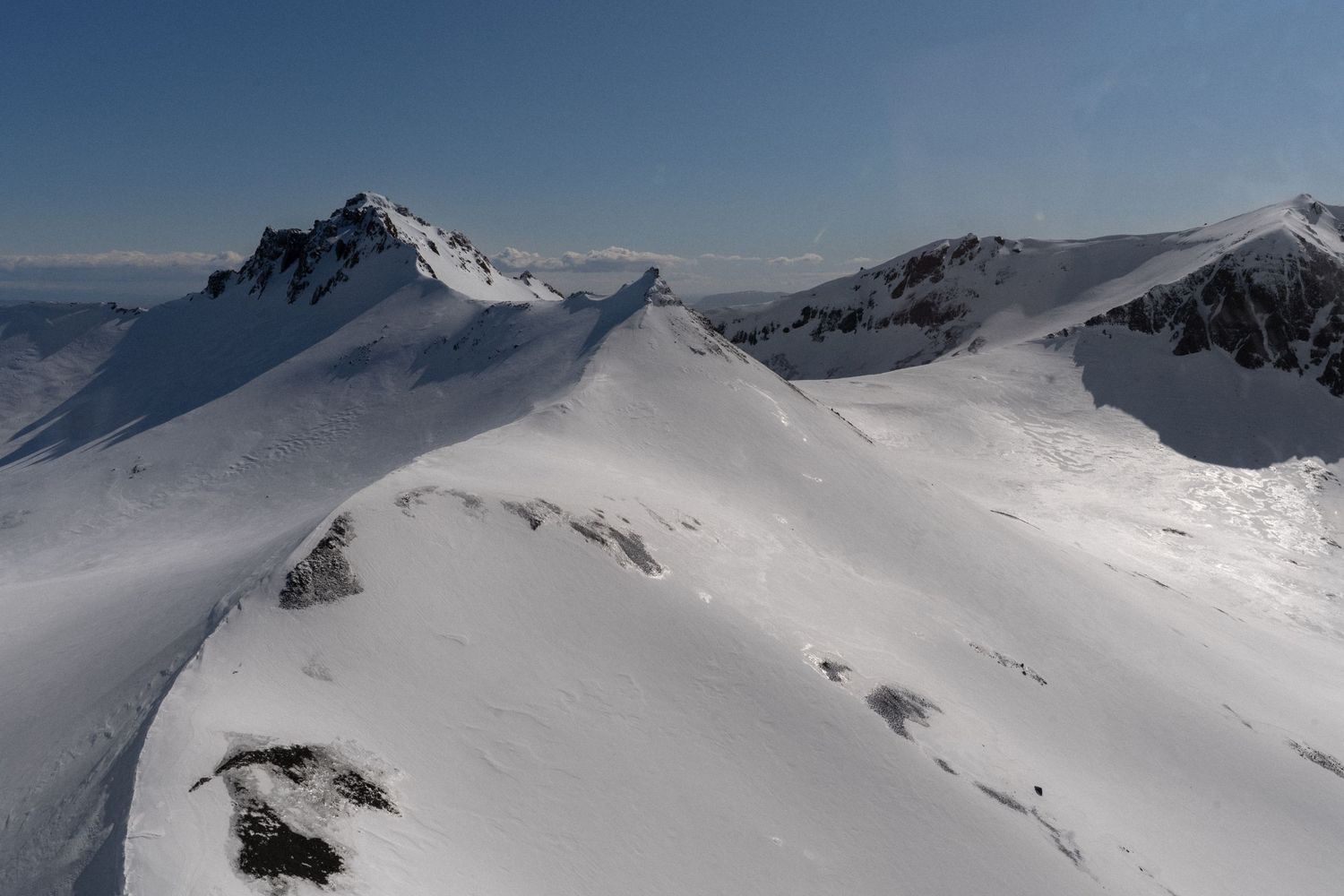Snow-covered mountain peaks and ridges stretch across a dramatic winter alpine landscape under bright sunlight.