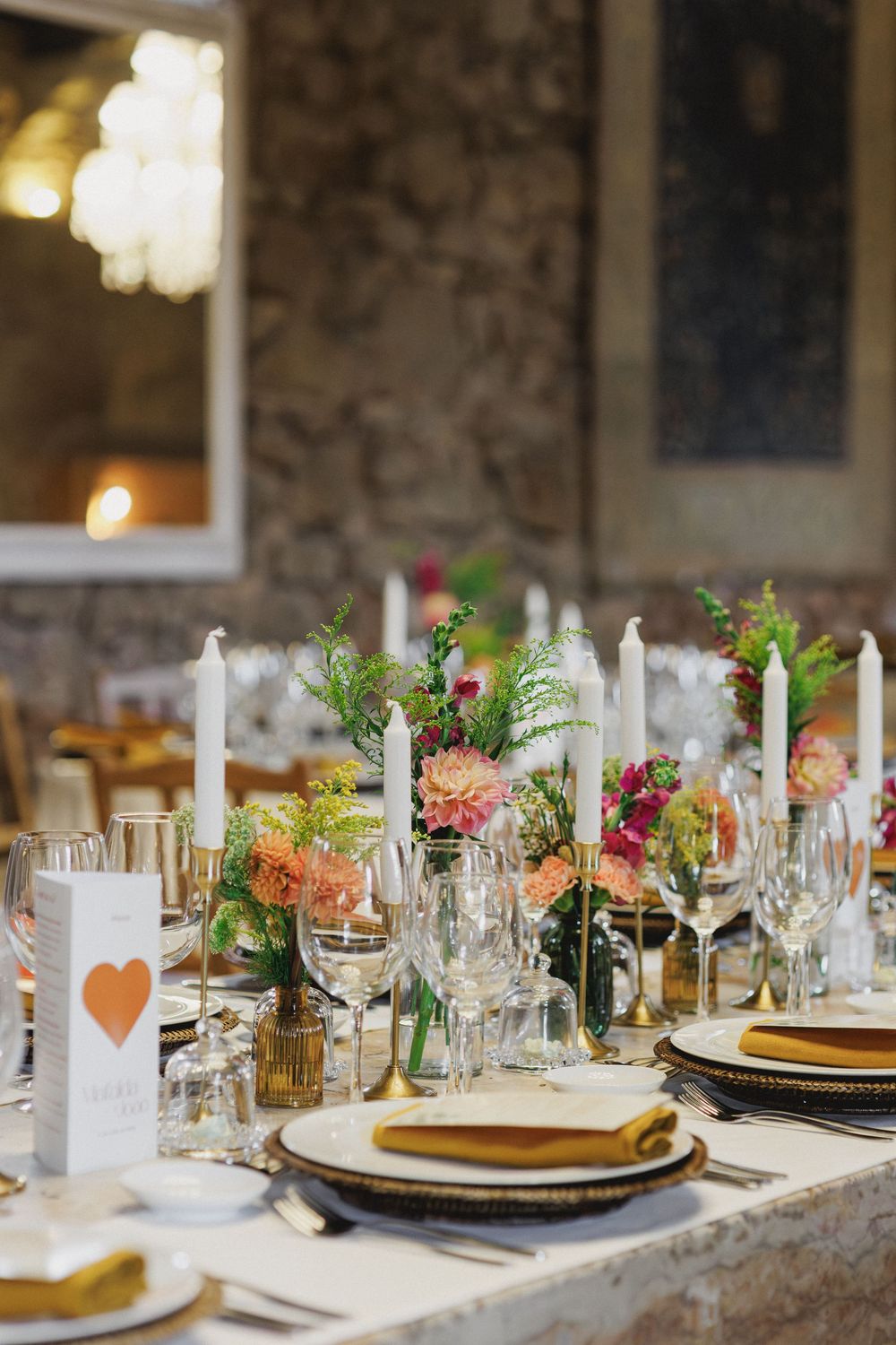 Elegant wedding table setting with gold chargers, white candles and coral floral centerpieces in a rustic venue in lisbon