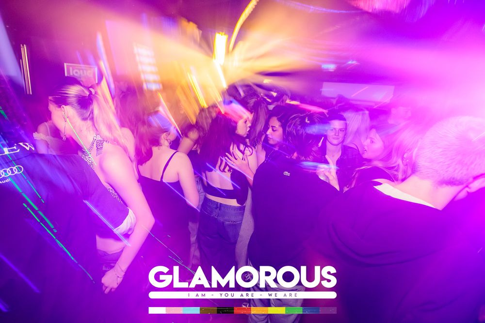 Crowded dance floor with pink and yellow lighting effects at Glamorous nightclub.