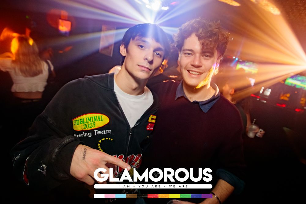 Two friends posing together under red lighting at Glamorous nightclub.