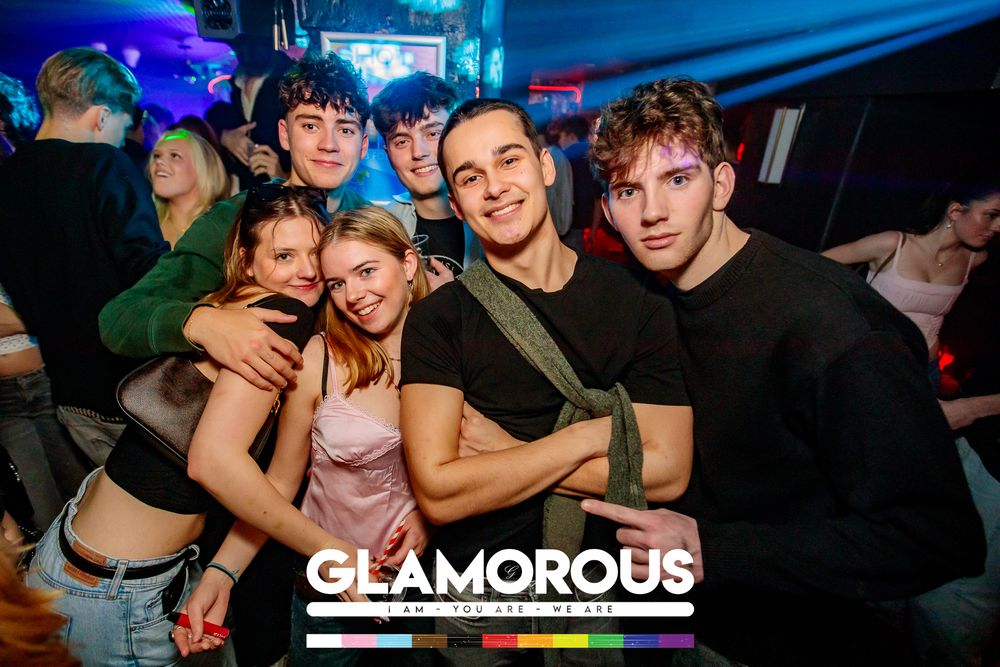 Group of friends posing together at a nightclub with blue lighting and Glamorous branding.