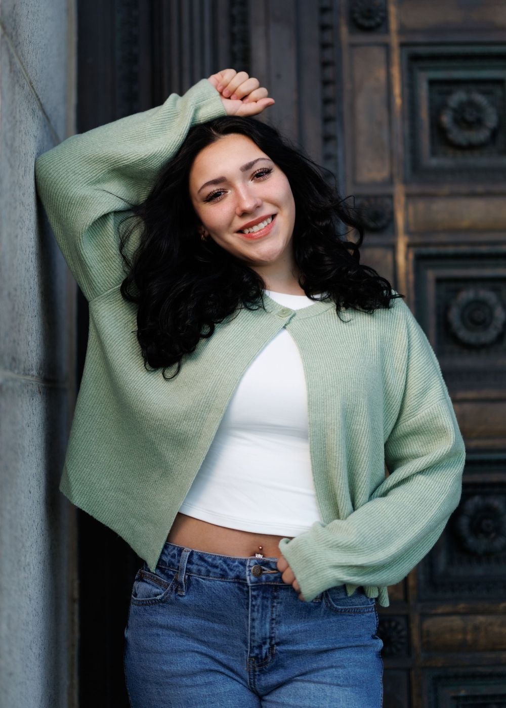 A girl in mint green sweater and jeans poses playfully against ornate door.