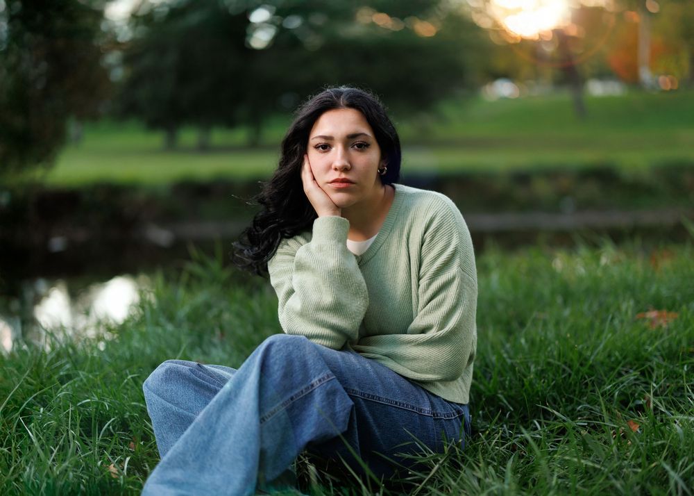 A graduate of Indian Valley high school in Gnadenhutten sits on grass at sunset near pond.