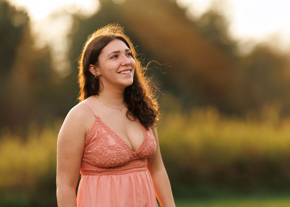 Person in coral dress smiling during golden hour photoshoot in nature.