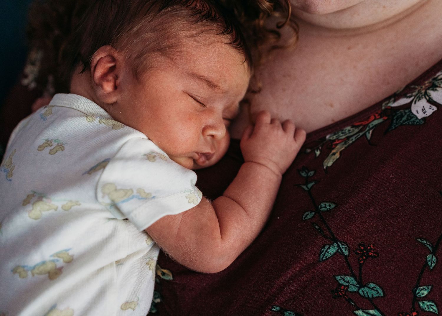 A sleeping baby in white clothing rests peacefully on a dark brown surface.