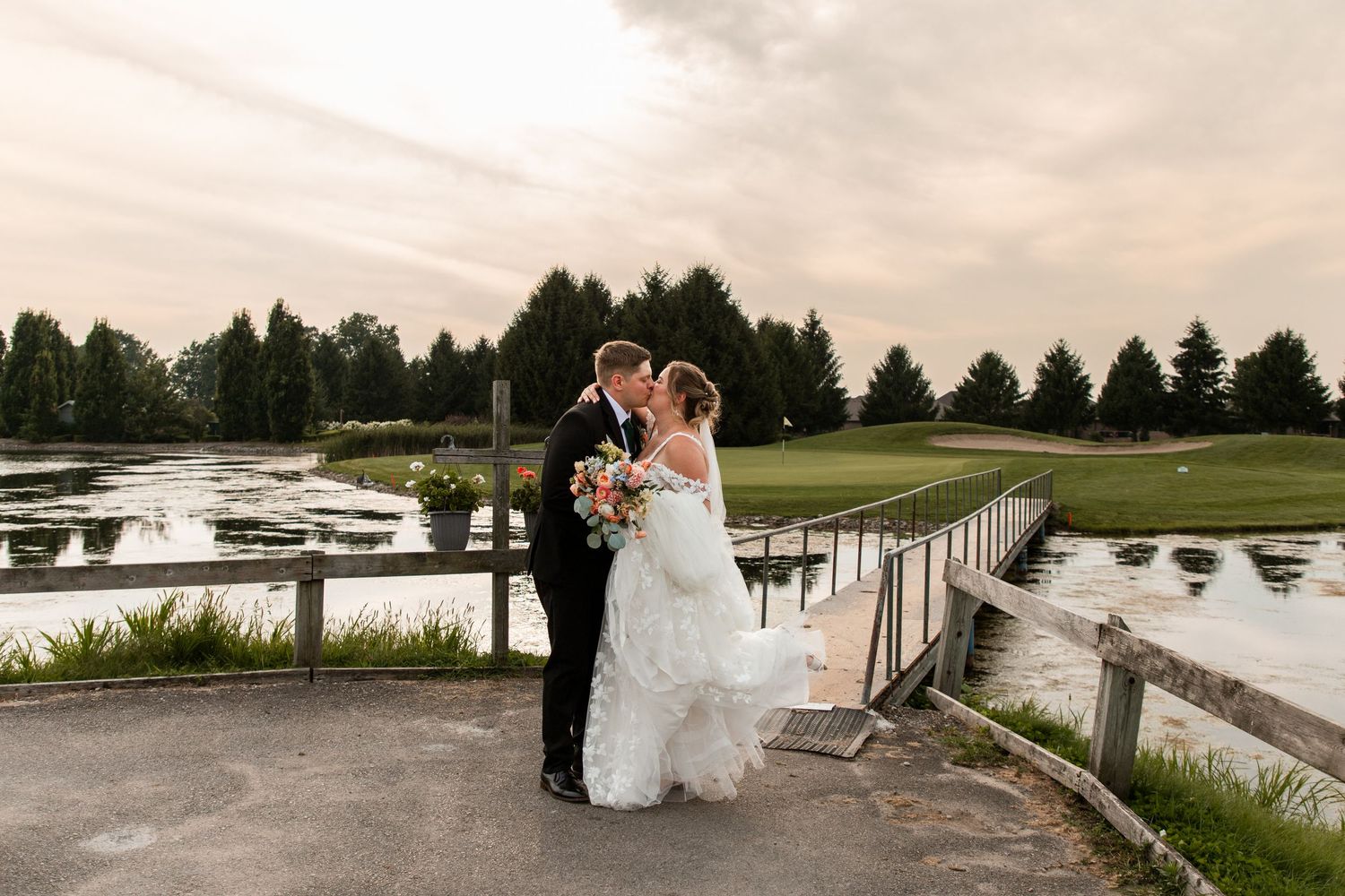 Newlywed couple poses for romantic wedding photos along a scenic waterfront dock at sunset.
