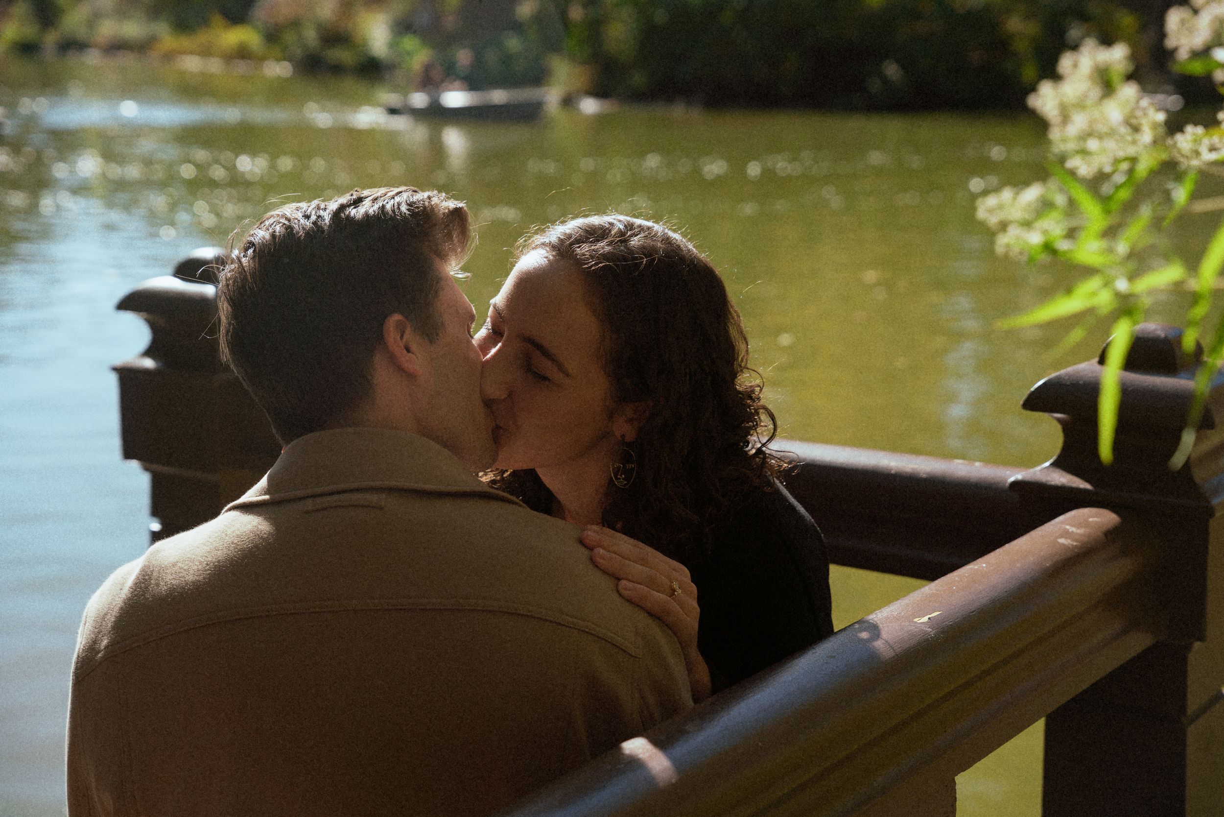 A romantic embrace shared between a couple on a park bench by a tranquil lake at sunset.