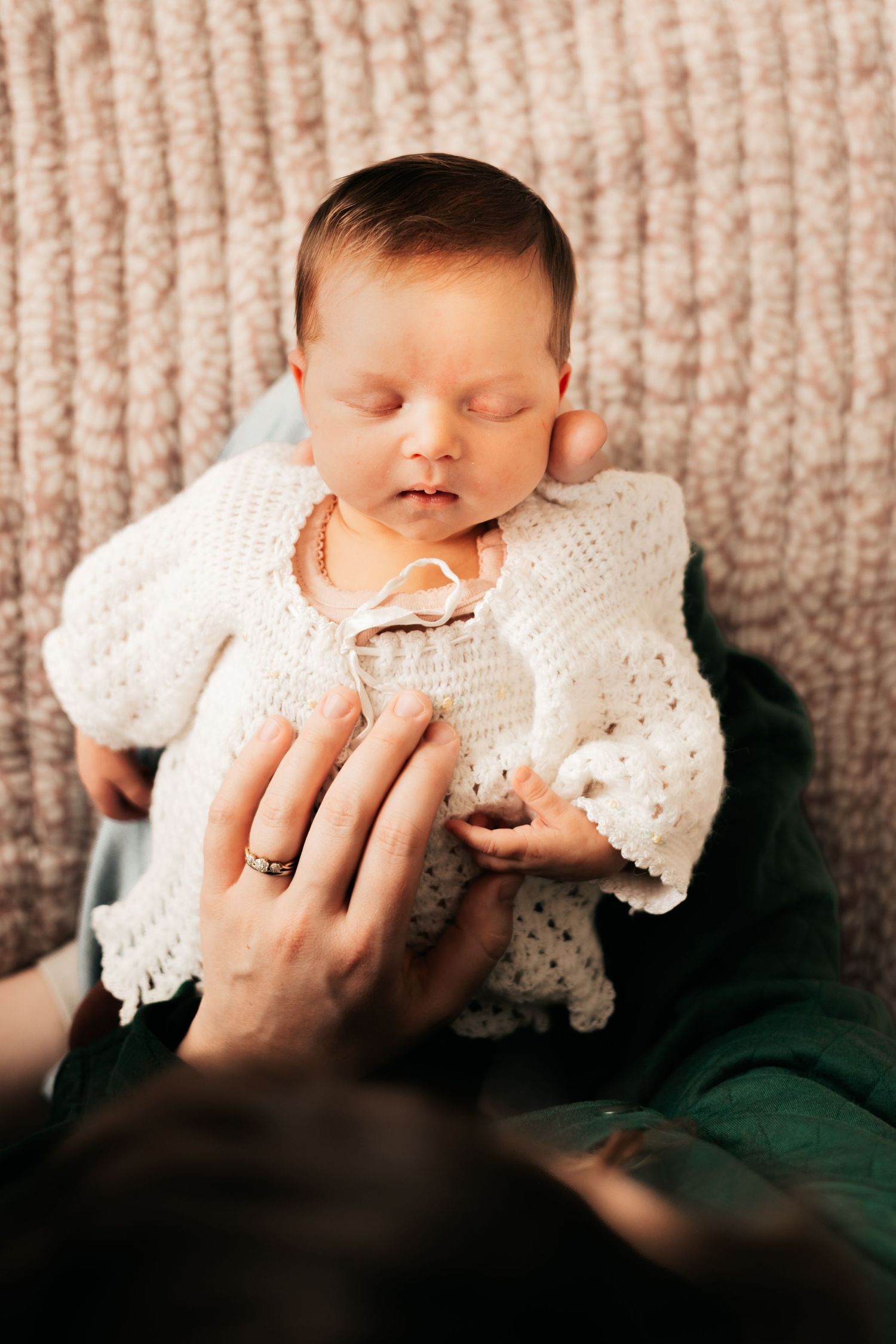 Newborn sleeping peacefully in white knit outfit cradled against a soft pink background |Newborn Photos When You Don't Feel Like Yourself