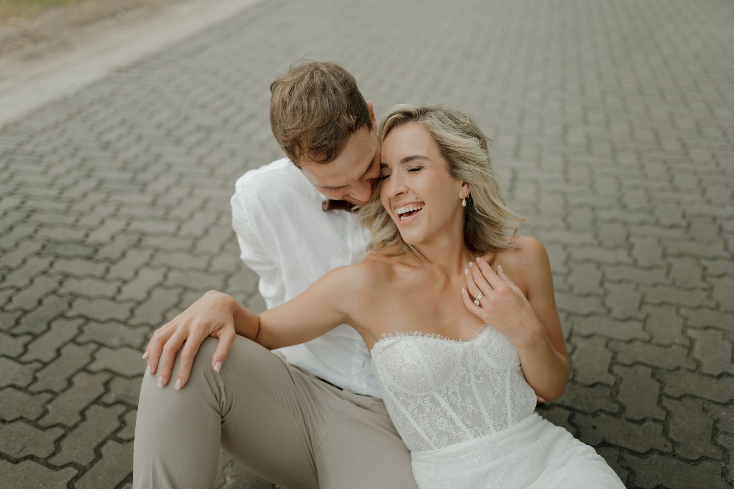 A romantic couple lying together on cobblestone pavement during a wedding photo session.