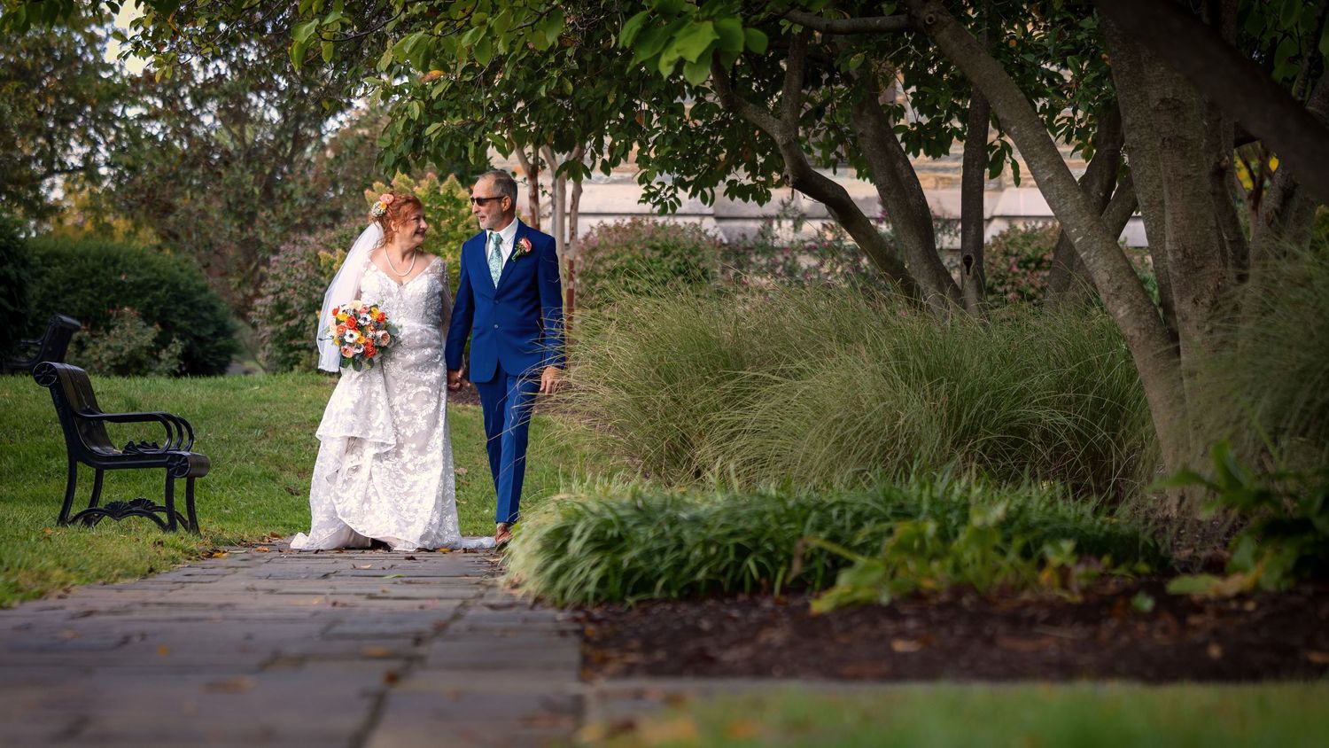 frederick maryland wedding photographer Couple walks together along garden path surrounded by trees and landscaping.