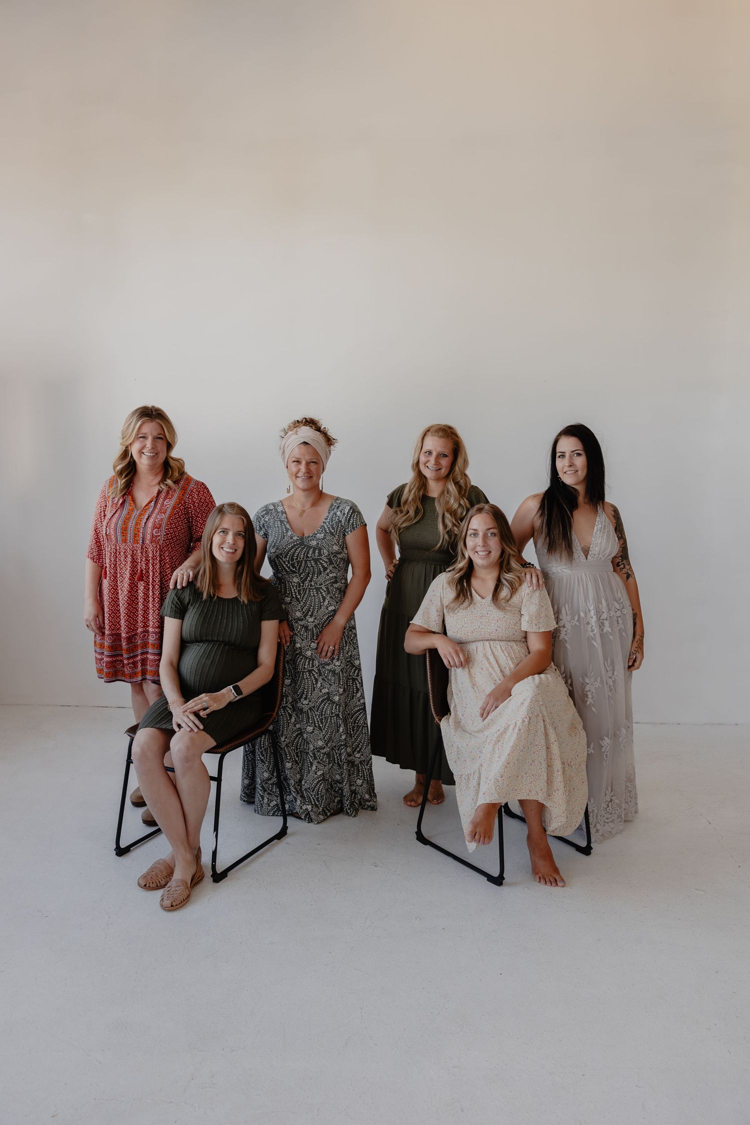 Group portrait of women wearing casual dresses and maxi dresses in neutral tones sitting against a light background.