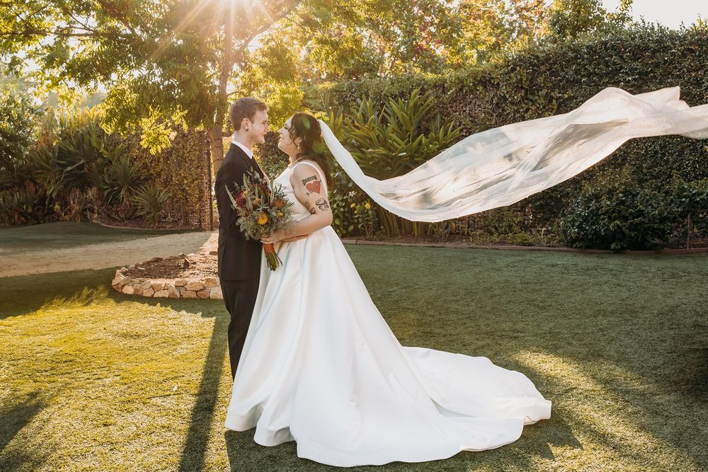 A flowing white wedding dress billows in the sunlight as the couple faces each other at River Garden Weddings and Events.