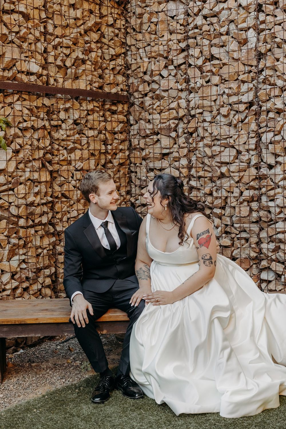 Newlywed couple sits together in front of a rustic stone wall background at River Garden Weddings and Events.
