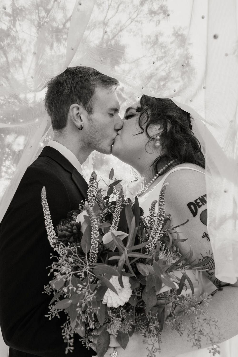 A romantic black and white wedding photo showing a couple kissing among delicate floral arrangements at River Garden Weddings and Events..