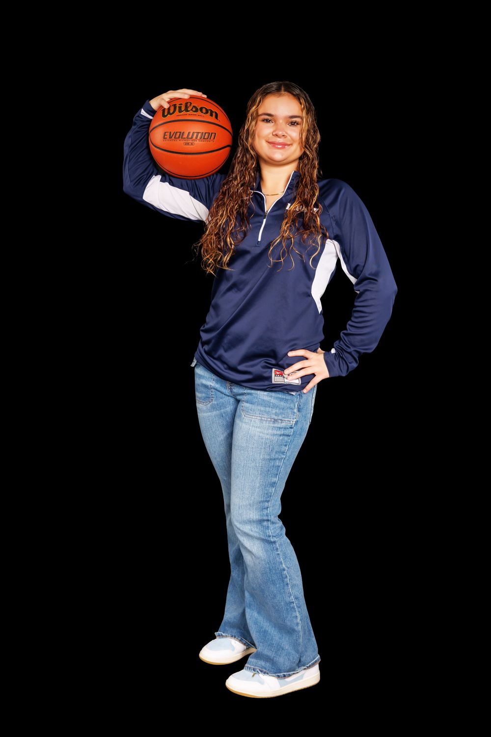 Player in navy sweater and jeans poses casually with basketball.