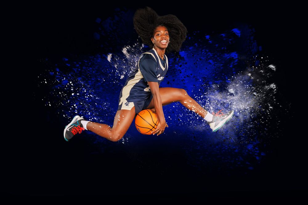 Dynamic basketball player leaping through the air with a ball against dramatic blue splashing background effect.