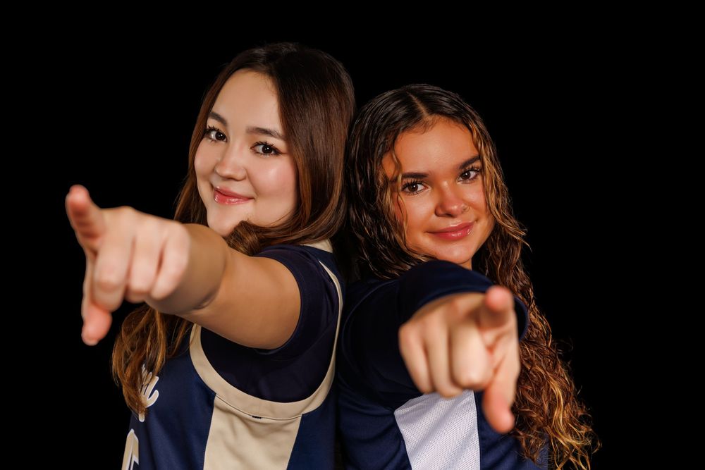 Athletes in navy uniforms point and pose playfully against black background.