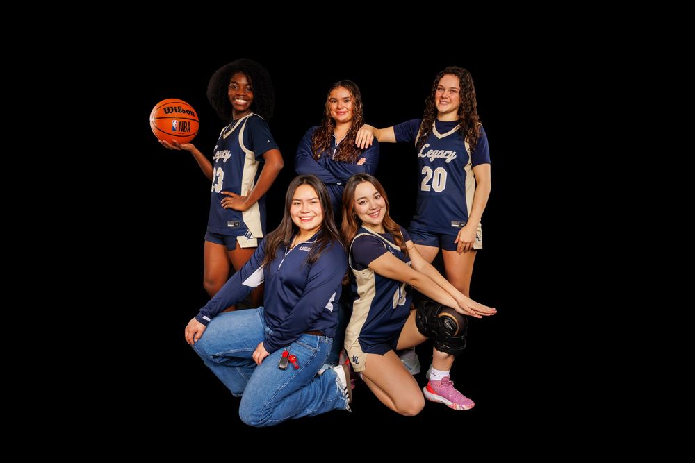 Basketball team members in navy uniforms pose together against black background.