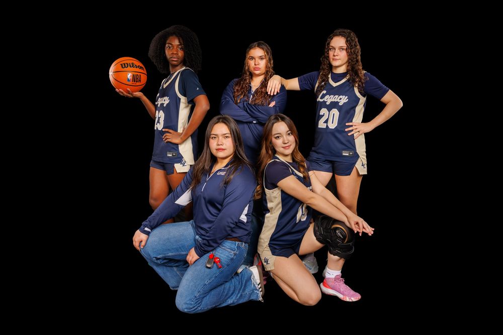 Basketball team members in navy uniforms pose together against black background.
