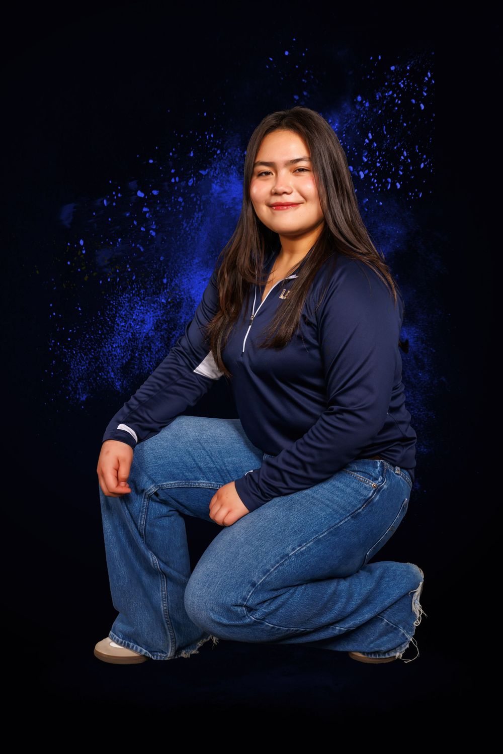 Athletic photoshoot against dark background featuring navy blue top and jeans with sparkly lighting effects.