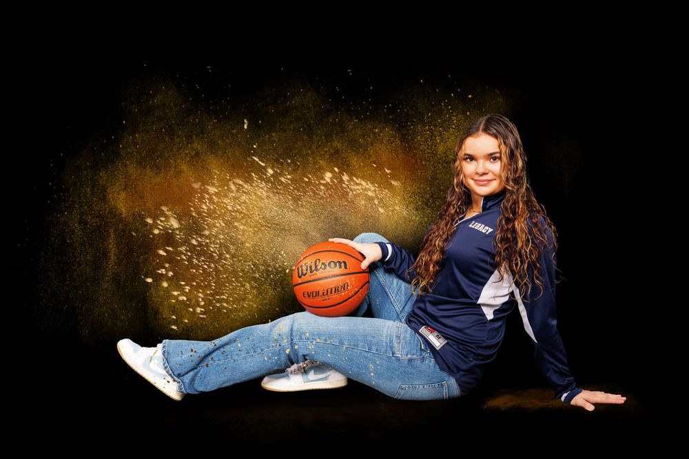Basketball player in navy uniform reclines with ball in artistic lighting.