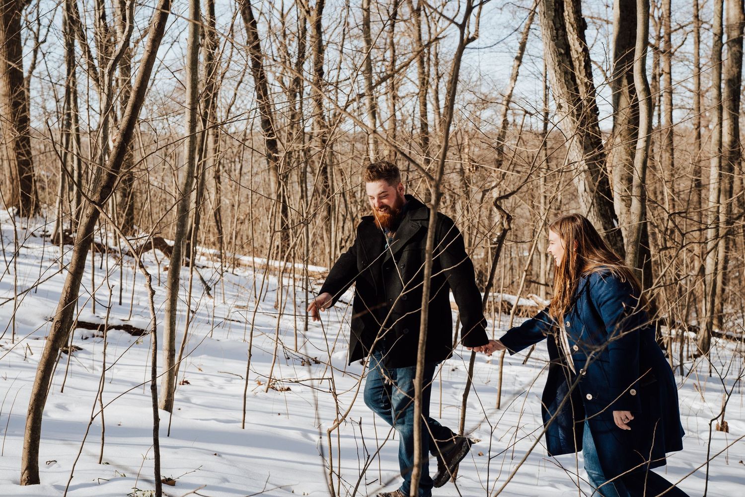 Two people hiking through a snowy winter forest trail for engagement photoshoot in Pequea, PA, Lancaster county.