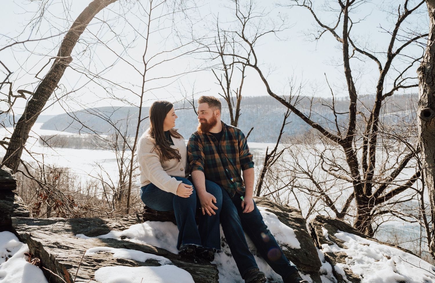 A couple poses for romantic engagement photos in a snowy winter landscape with mountain views.