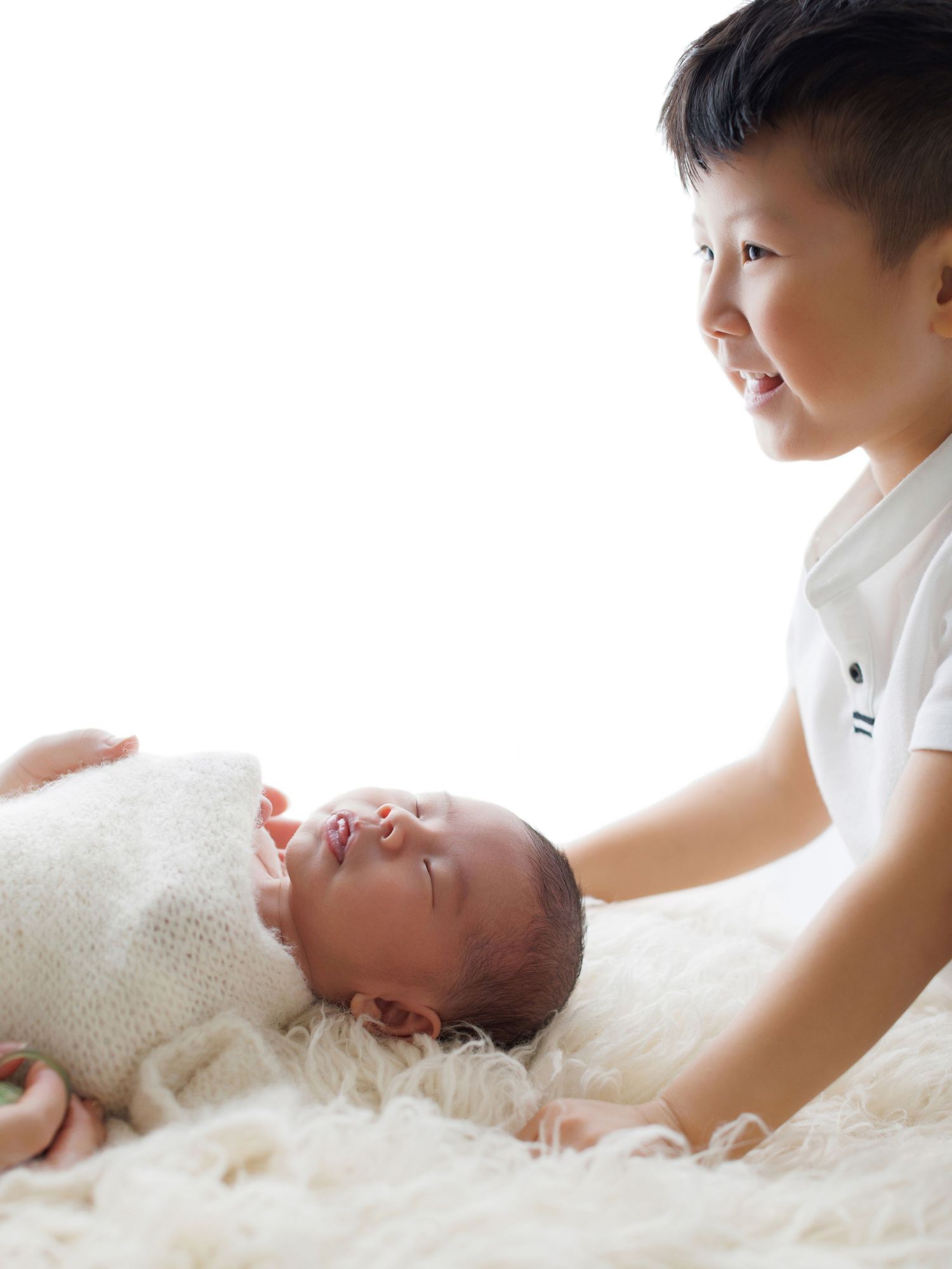 A tender moment captured as a baby lies on soft white bedding while being gently touched.