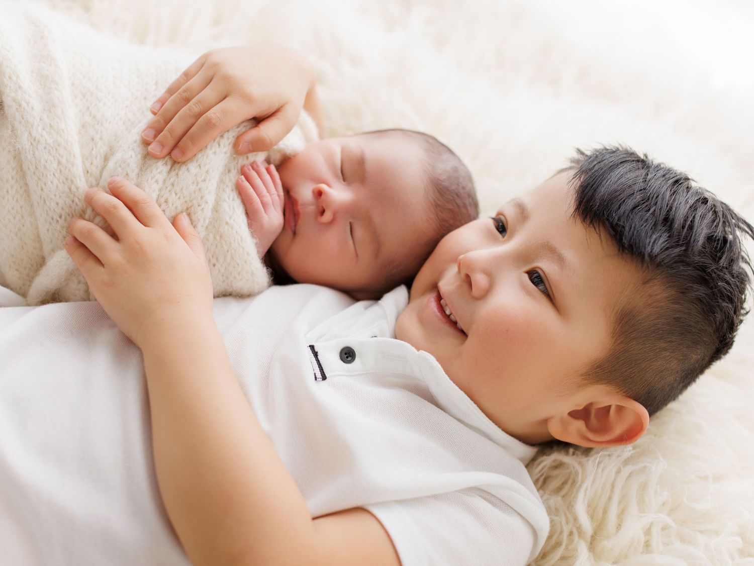 Two siblings sharing a sweet bonding moment while resting together on plush white fur.