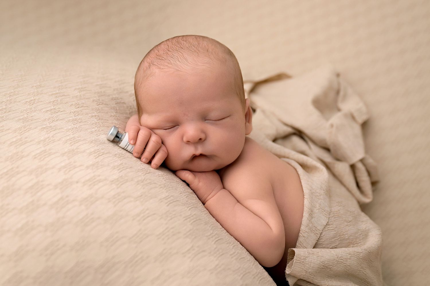 A sleeping newborn baby wrapped in beige blankets on a neutral backdrop.