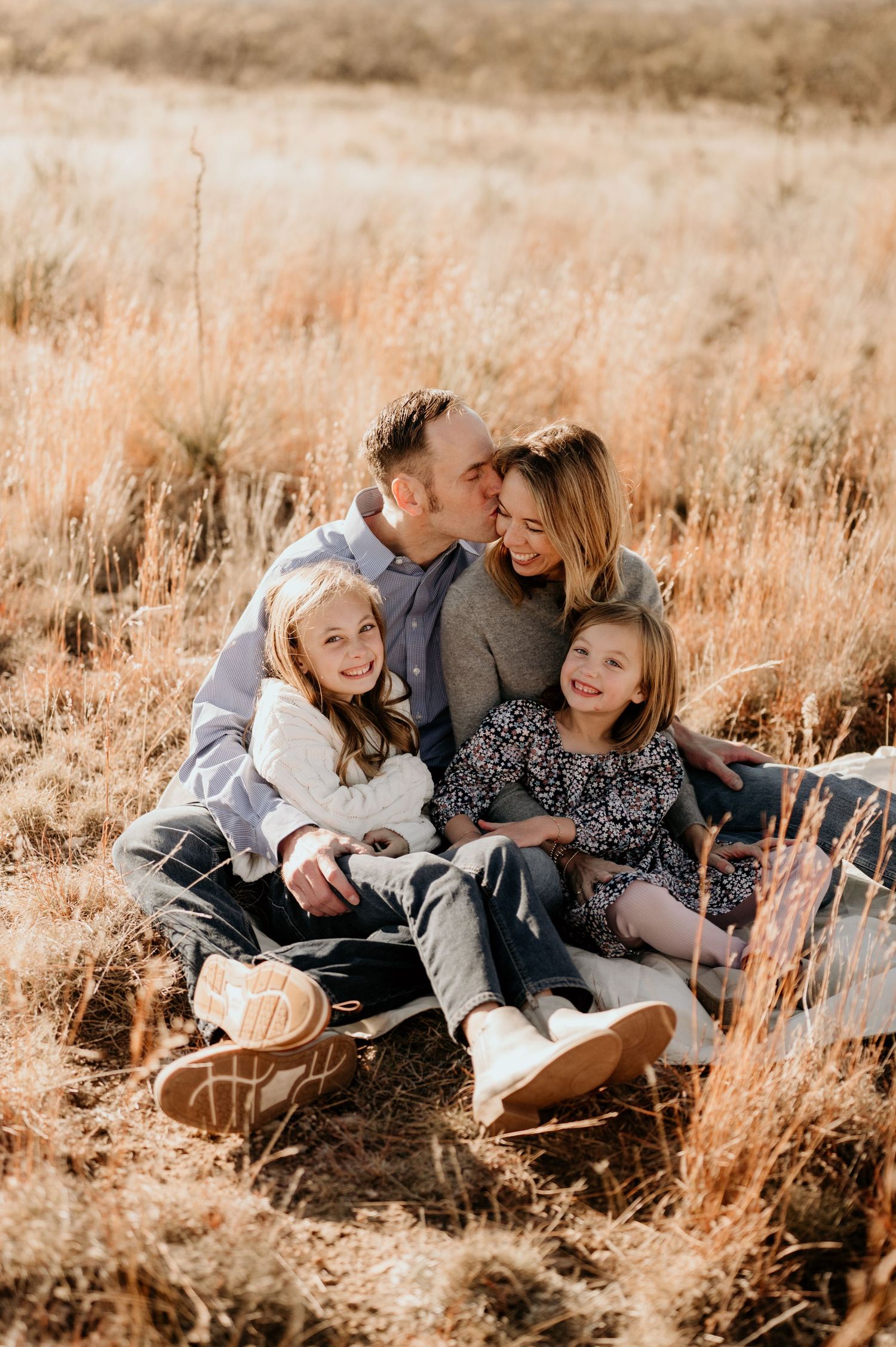 Family lying together in golden autumn grass during sunset photo session.