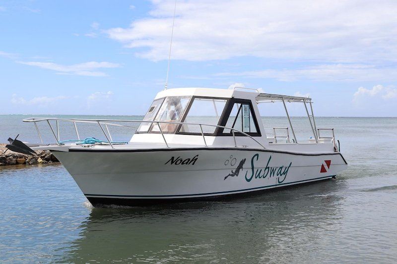 White cabin cruiser boat moored near rocky coastline on calm waters.