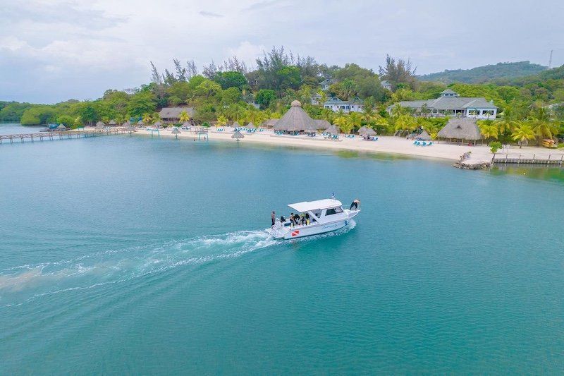 Aerial view of luxury boat cruising through turquoise waters near tropical island coastline.