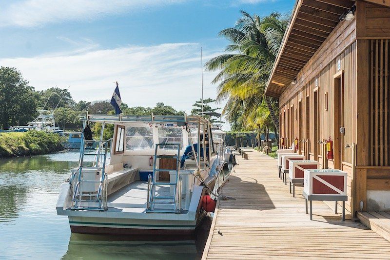 Marina boardwalk with docked boats and waterfront buildings under blue skies.