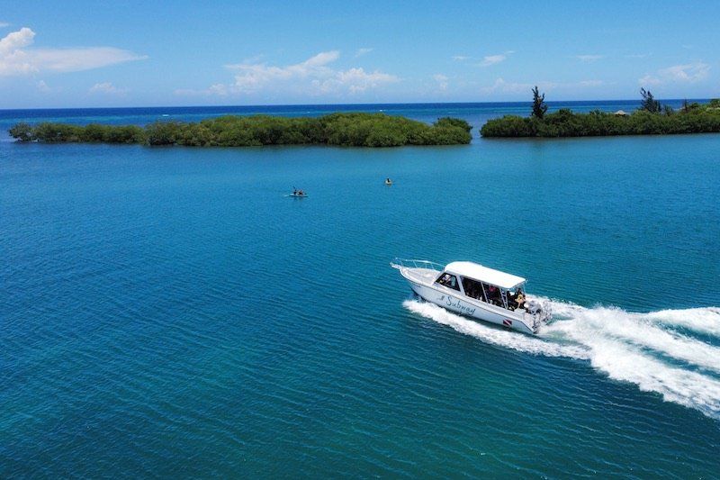 Aerial view of white boat speeding through pristine blue waters between tropical islands.