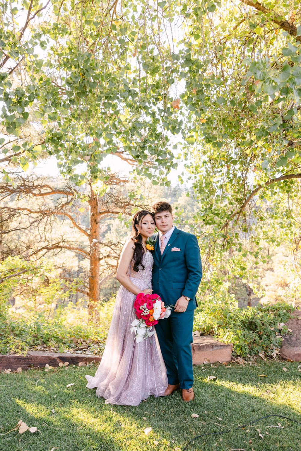 A romantic couple shares tender moments in a sunlit garden setting with autumn trees and red flowers.