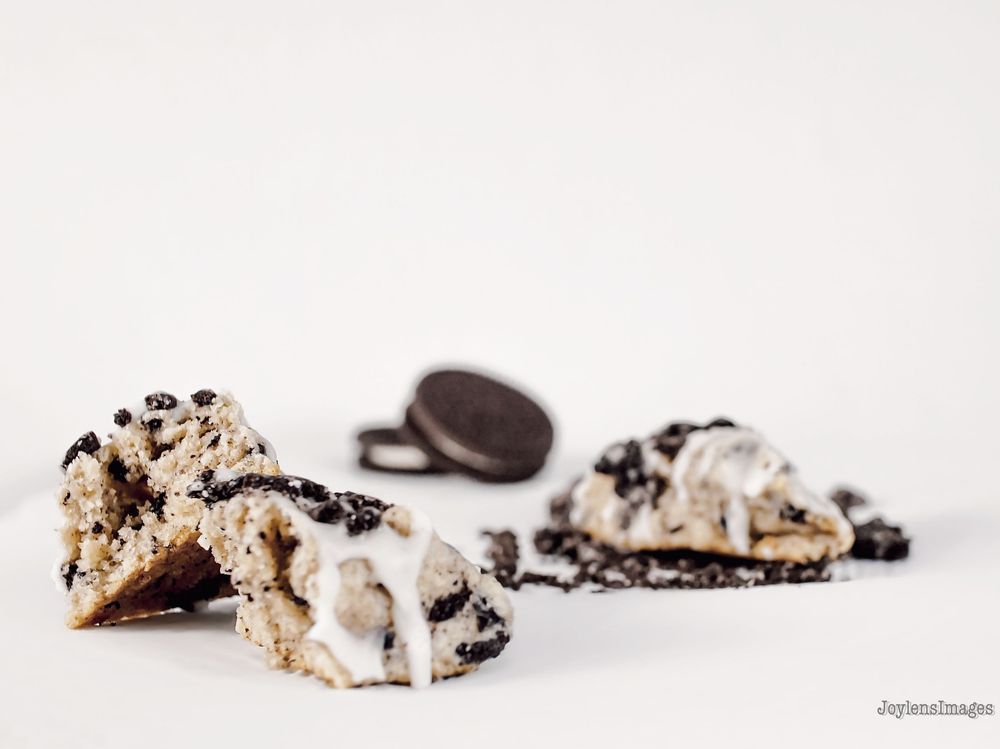 A broken Oreo cookie with cream filling lies scattered in pieces across a white surface.