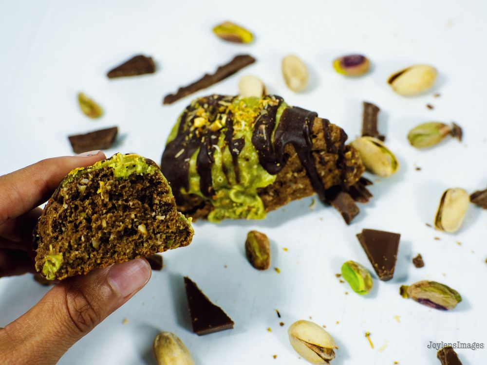 Dark chocolate pistachio biscotti with green nuts scattered on a white surface shows texture and crunch.