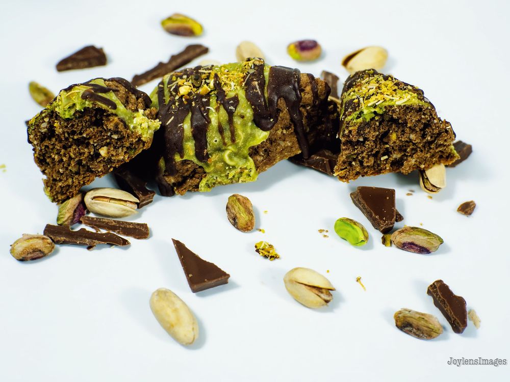 Dark chocolate bark pieces with green pistachio nuts scattered on a white surface.