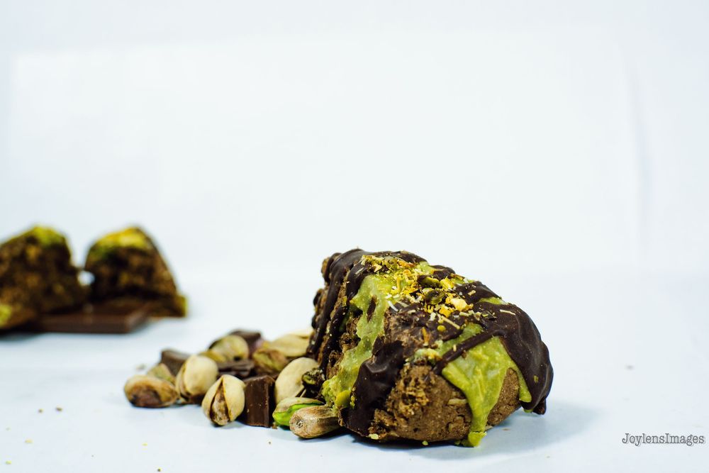 Chocolate dipped pistachio cookies arranged in a line on a white surface showing different angles and textures.