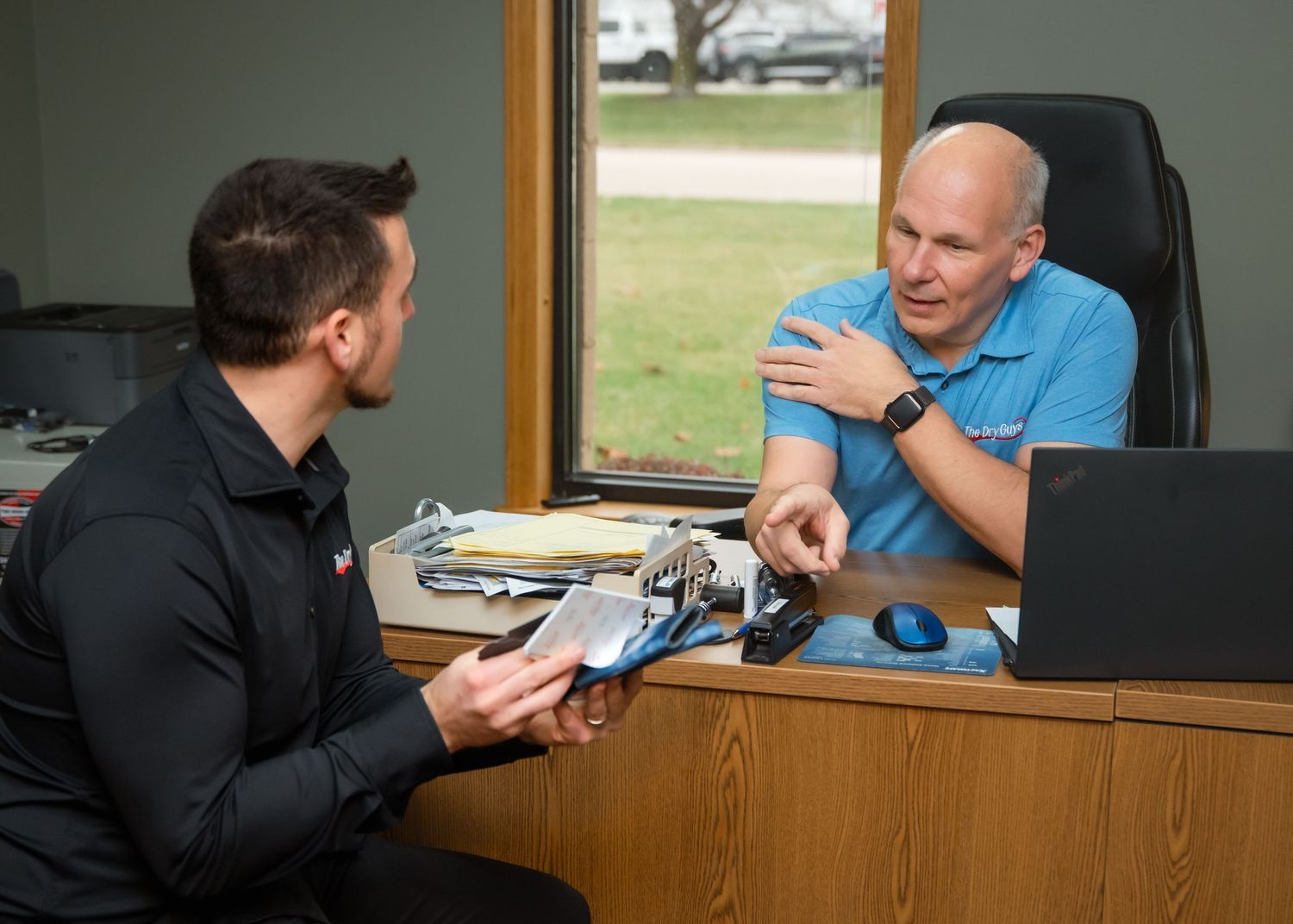 Two people sit at a desk in an office environment engaged in conversation during a business meeting.