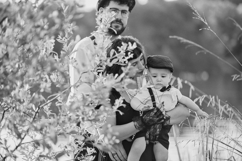 Black and white photo of bearded father holding baby and toddler among wildflowers.